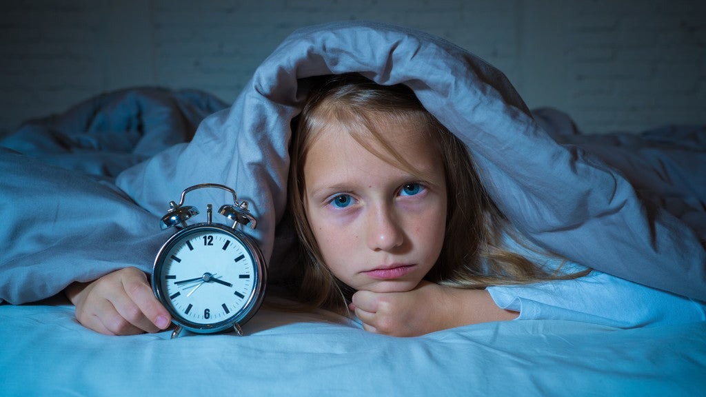 Cute Sleepless little girl in bed holding clock
