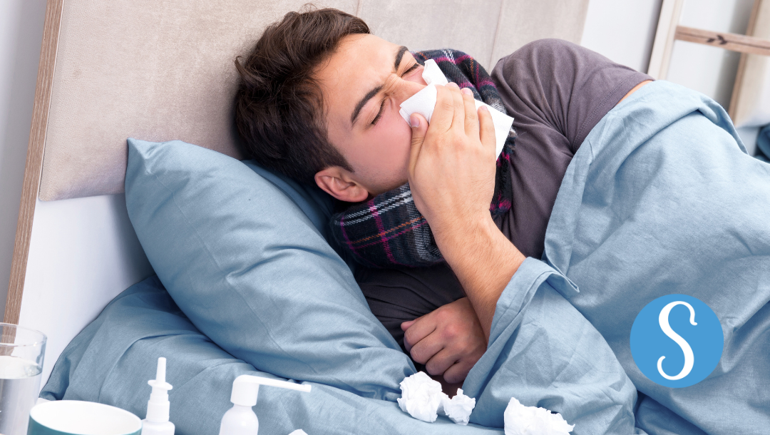A man lying in bed, sick and blowing his nose.