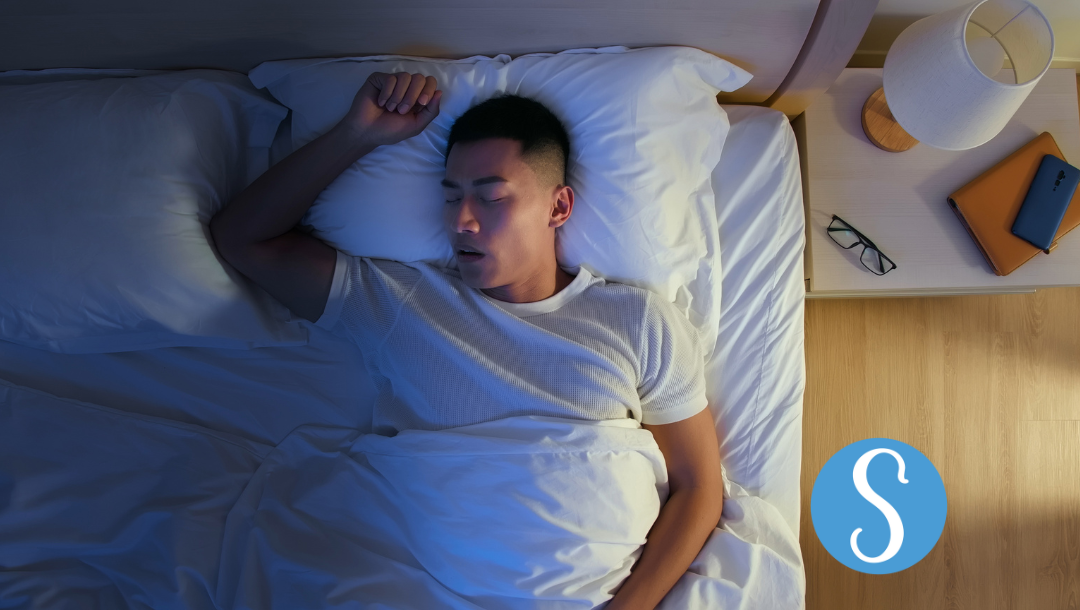 A man sleeping in bed on his back, snoring.